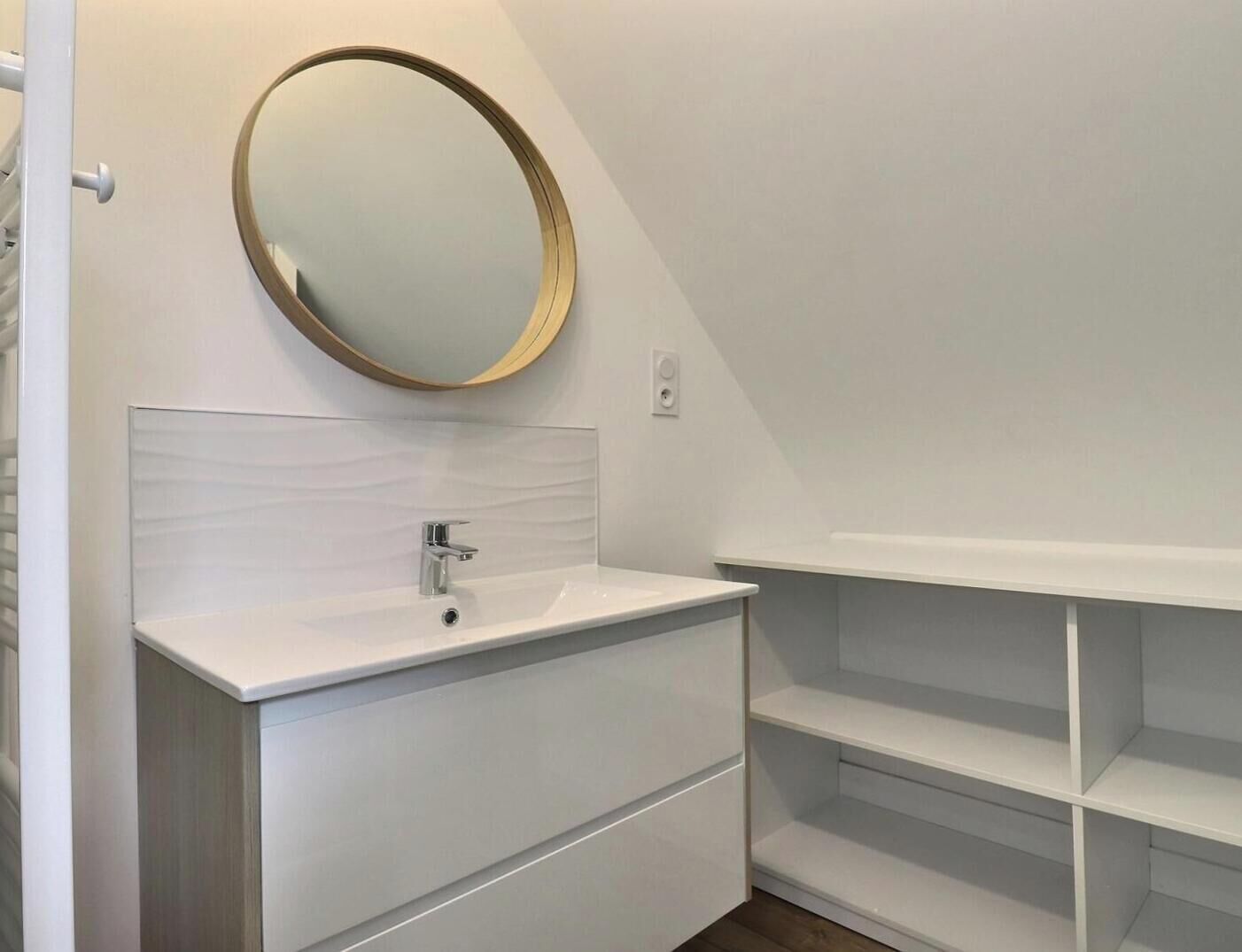 Een moderne badkamer met een wit wastafelmeubel, een ronde spiegel en ingebouwde planken.