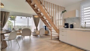 Une cuisine moderne avec un escalier en bois, un coin repas avec des chaises et une vue dégagée grâce à de grandes fenêtres.