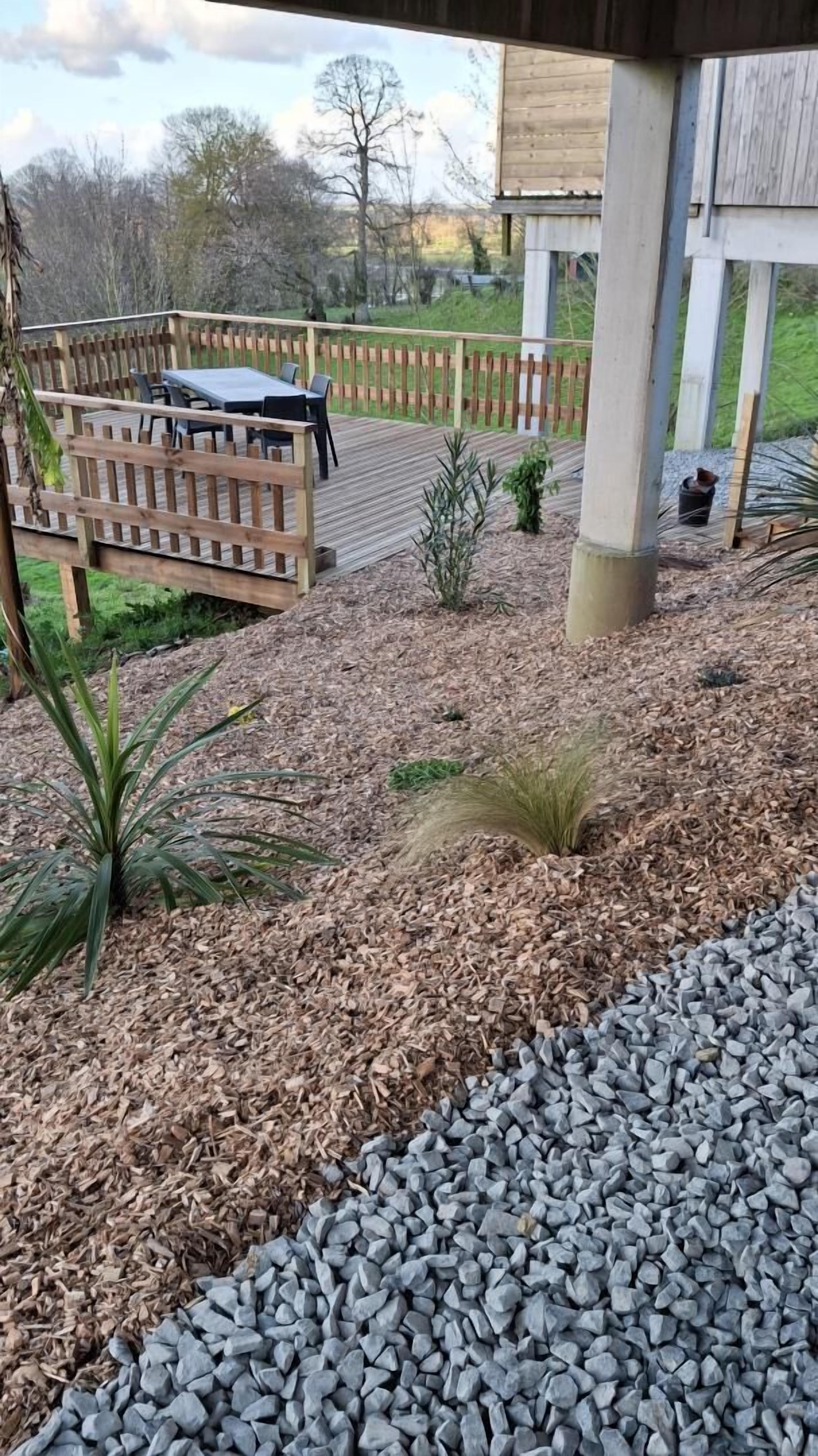 Une terrasse en bois, agrémentée de mobilier d’extérieur, entourée de paillis et de gravier.