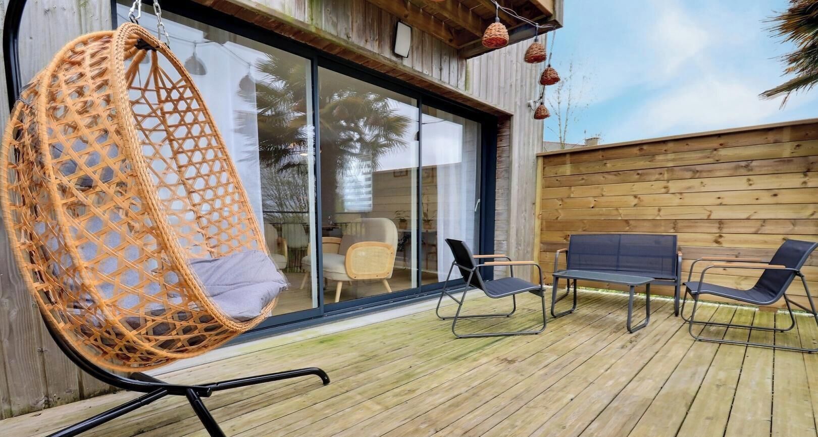 Une terrasse en bois avec un fauteuil suspendu, deux chaises longues et un banc.