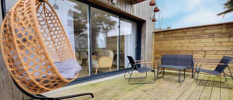 A wooden deck with a hanging chair, two lounge chairs, and a bench.