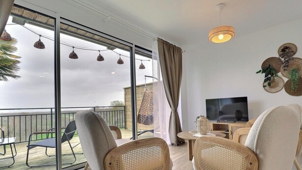 Un balcon avec des fauteuils en osier, un téléviseur et un luminaire suspendu.