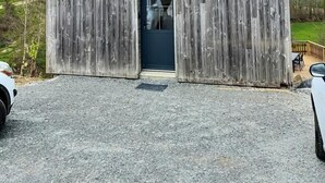 Une grange en bois avec une porte sombre et deux fenêtres, une allée gravillonnée et un espace extérieur clôturé.