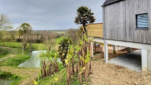 Un bâtiment rustique en bois, doté d’un balcon donnant sur un étang et la verdure environnante.