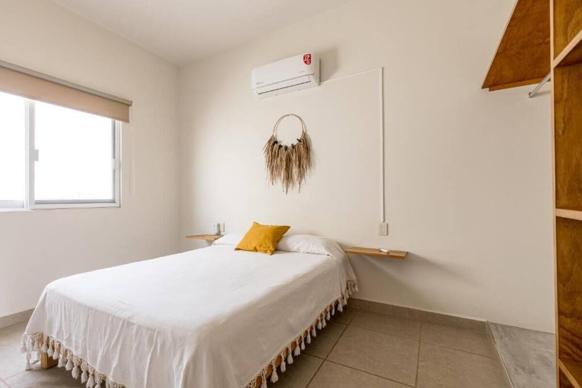 Une chambre à coucher comprenant un lit, une table de chevet, un climatiseur fixé au mur et une fenêtre avec un store.