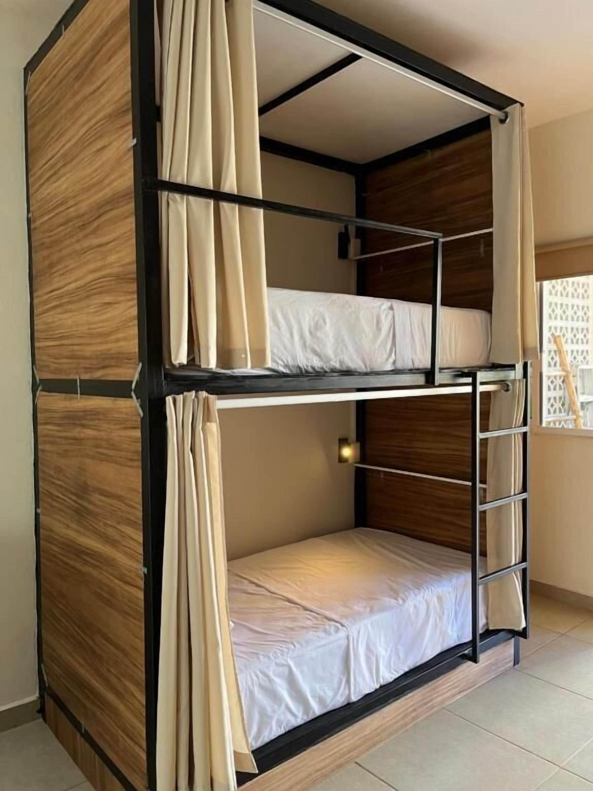 Una cama litera con estructura de madera, una escalera y cortinas.
