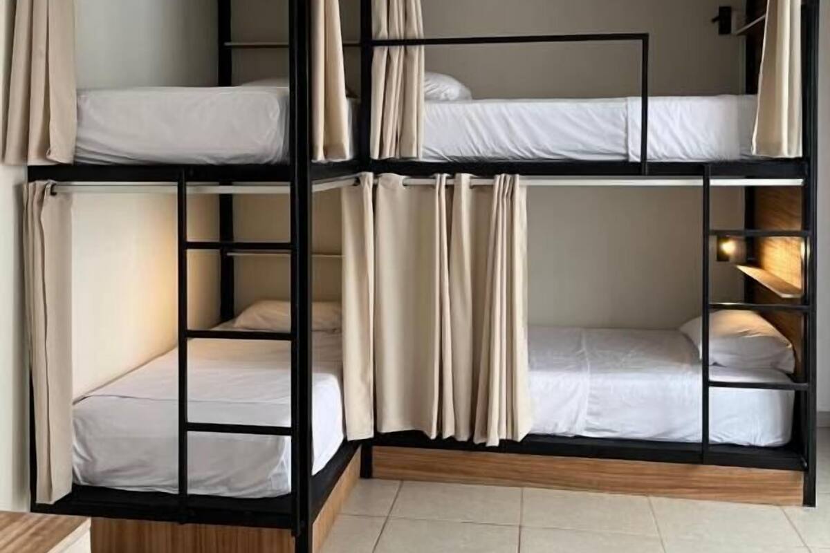 Une chambre avec des lits superposés, des rideaux, une table en bois et un sol carrelé.