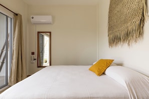 A bedroom with a bed, a window with curtains, an air conditioning unit, and a wall-mounted woven tapestry. - Bahía Sirenas (Puerto Escondido)