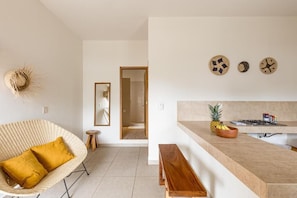 A modern kitchen with a wooden bench, a wicker chair with cushions, and a wall-mounted clock. - Bahía Sirenas (Puerto Escondido)