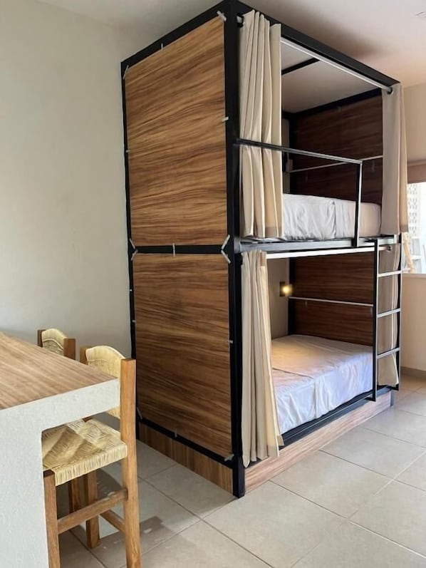 A bunk bed with curtains, a wooden table, and chairs in a room with tiled flooring. - Bahía Sirenas (Puerto Escondido)