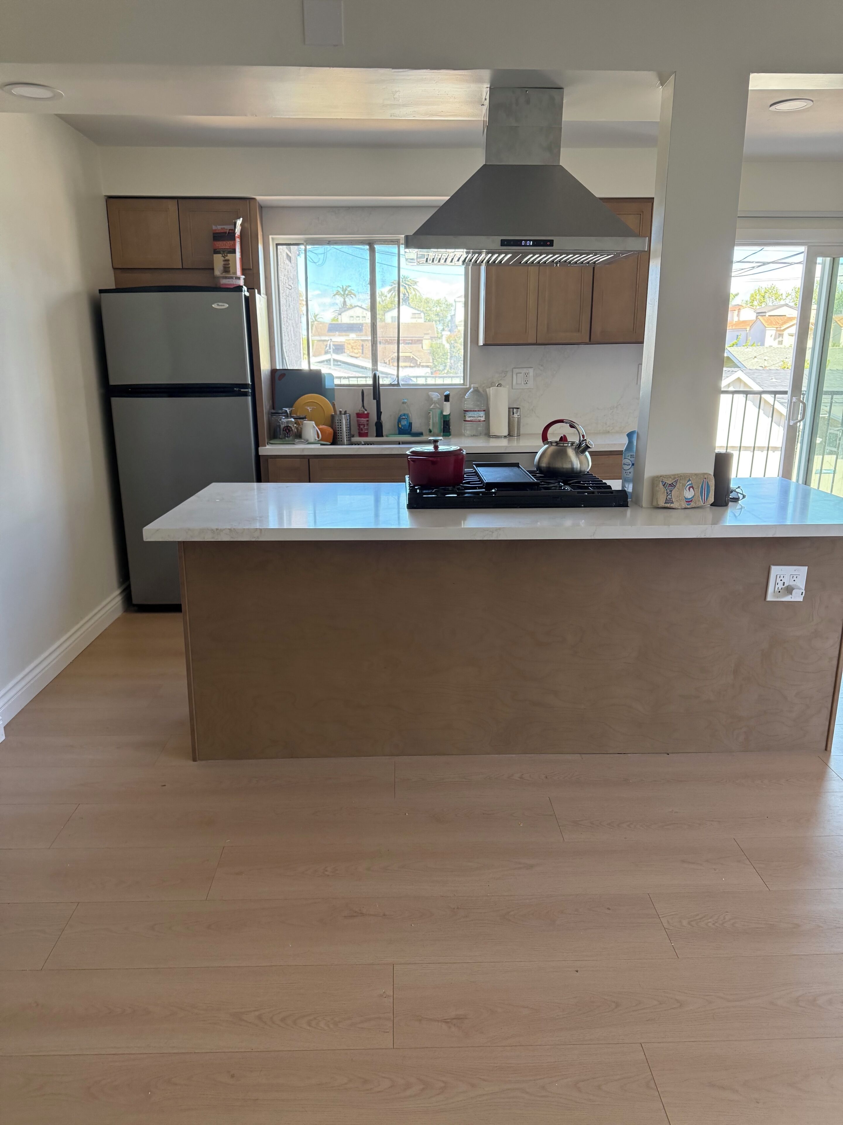 A modern kitchen with a central island, stainless steel appliances, and a large window providing a view of the outside.