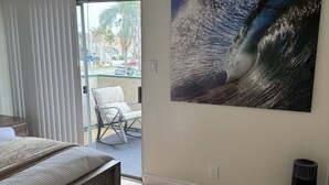 A bedroom with a bed, a large window, a painting of a wave, and a heater.