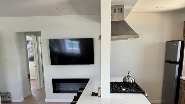 A modern kitchen with a central island, a built-in stove, and a flat-screen TV mounted on the wall.