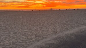 A beach with a sunset, sand, and distant structures.