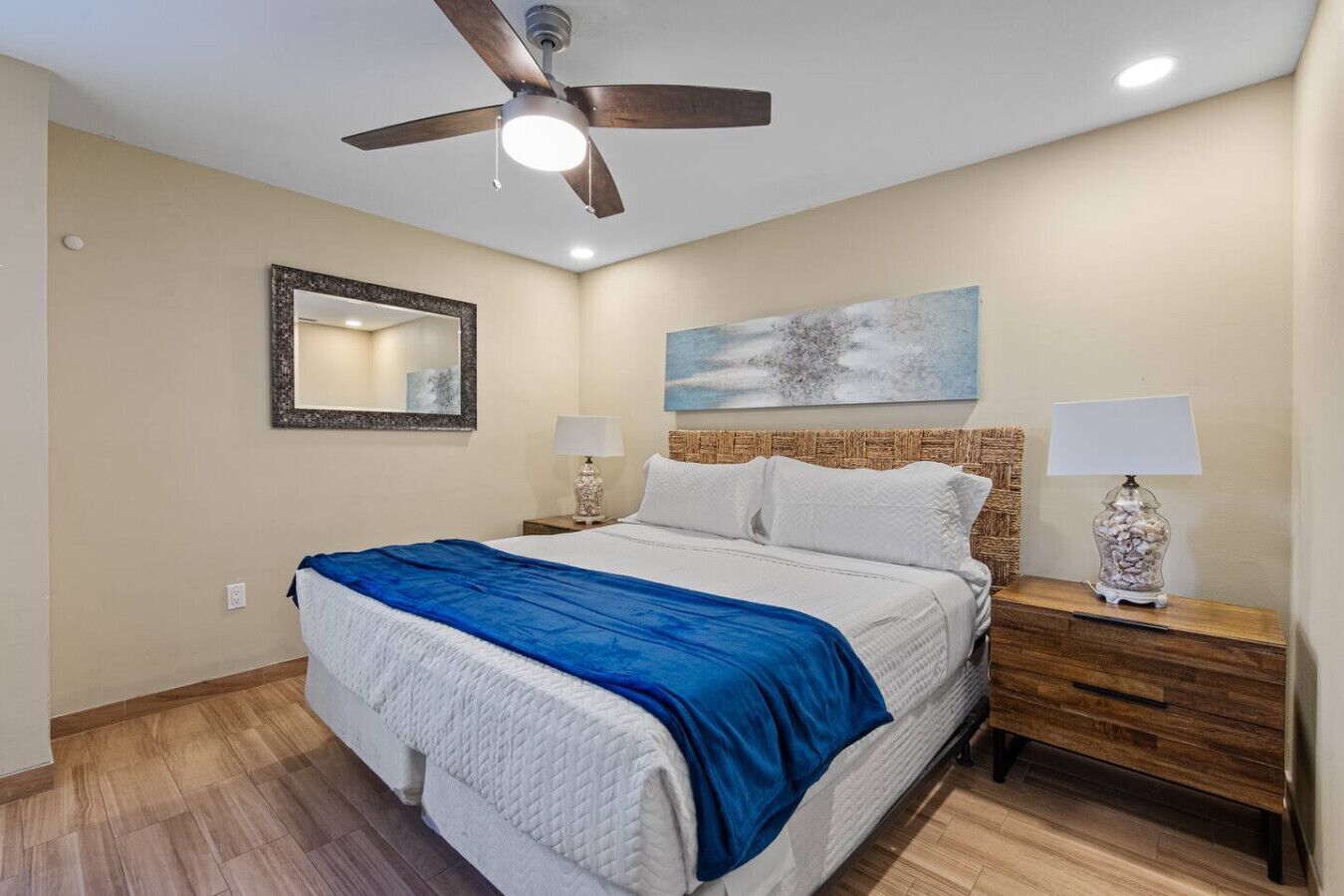 Ein Schlafzimmer mit einem Bett, Nachttischen, einem Deckenventilator, einem Spiegel und einem Bild an der Wand.