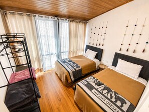 Ein Hotelzimmer mit Etagenbett, Schreibtisch und Stuhl, Fenster mit Vorhängen und Wand mit Dekoration.