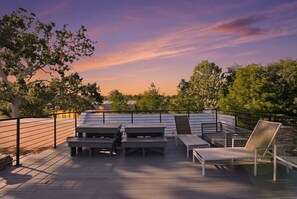 Una terraza al aire libre con asientos y vistas a árboles y una puesta de sol.