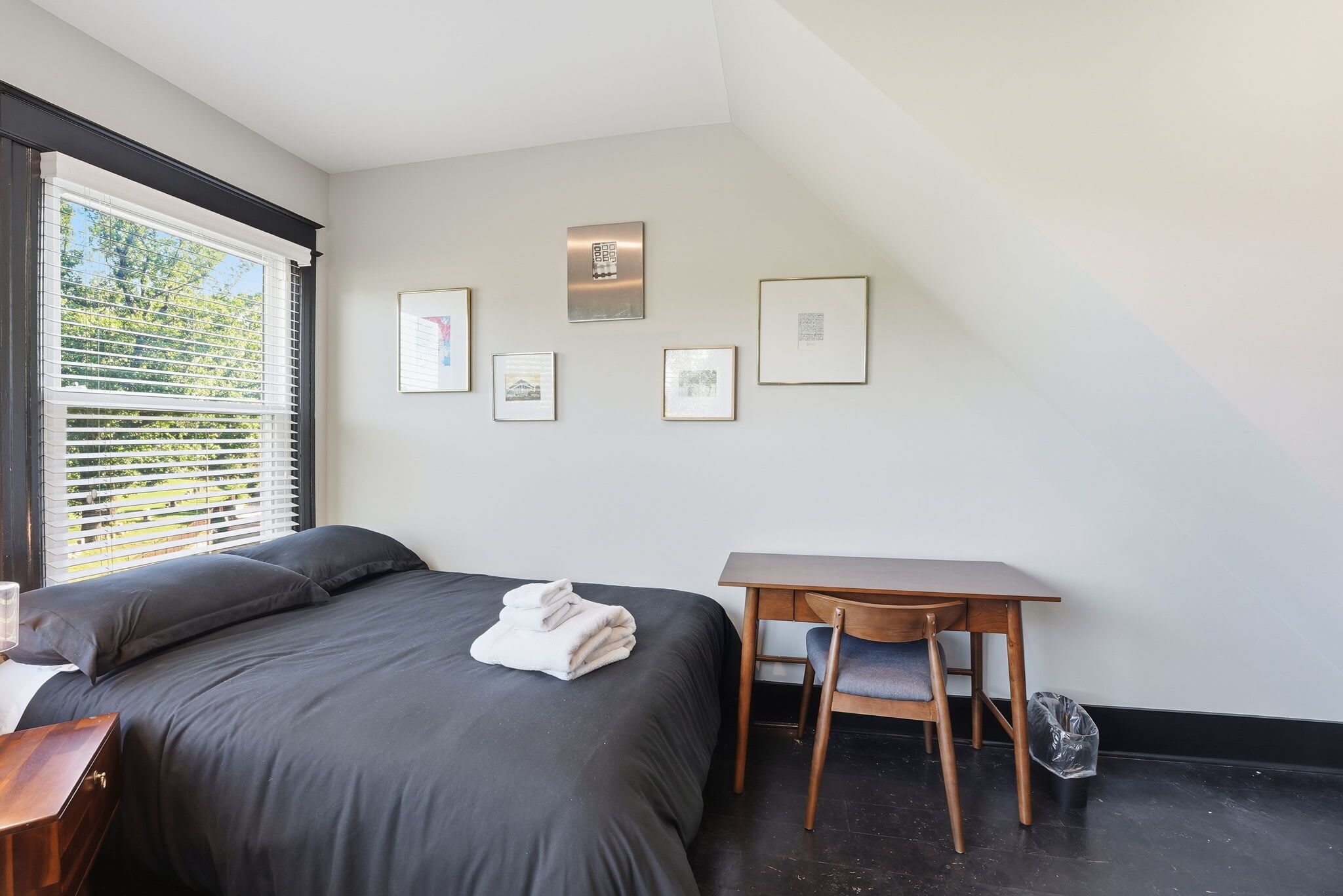 Une chambre à coucher avec un lit, un bureau et une chaise. Des tableaux encadrés ornent le mur.
