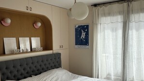 A bedroom with a tufted headboard, a bed with a white duvet, a ceiling fan, and a wall-mounted shelf with framed pictures and a map. - Modern, family-friendly Parisian apartment (Paris)