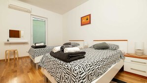 Ett hotellrum med två sängar, en liten pall, en spegel, ett fönster och en tavla på väggen.