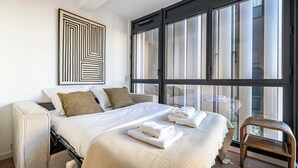 Un hotel moderno con una cama grande, vistas a través de ventanales del suelo al techo, una obra de arte colgada en la pared y un área de descanso junto a la ventana.
