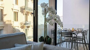 Un balcón con sofá, mesa de comedor, sillas y una orquídea en maceta.