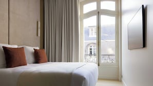 Ein Schlafzimmer mit einem Bett, zwei Kissen, einem Fenster mit Vorhängen und einer Tür zu einem Balkon.