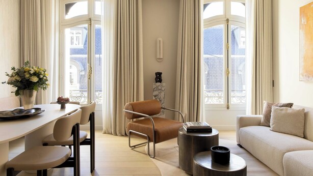 Ein modernes Wohnzimmer mit einer Couch, einem Esstisch mit Stühlen, einem Couchtisch und einem Fenster mit Vorhängen.