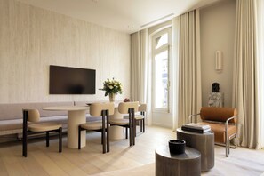 A modern living room with a sofa, dining table, chairs, a TV, a vase with flowers, and a statue. - Luxury Flat -2br/6p- Madeleine/saint Honore (Paris)