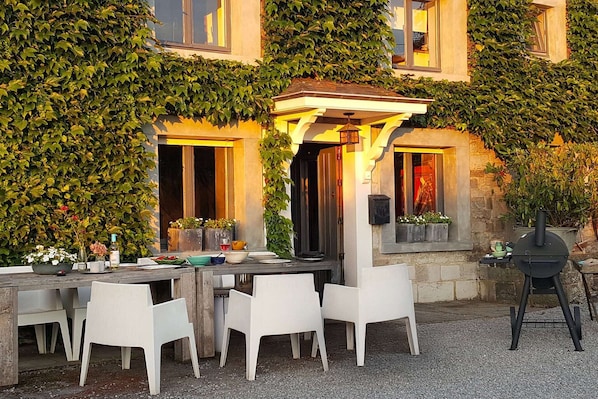 An outdoor dining area with a table and chairs, a grill, and a building covered in ivy. - Charming Garden Holiday Home for 6 (Weris)