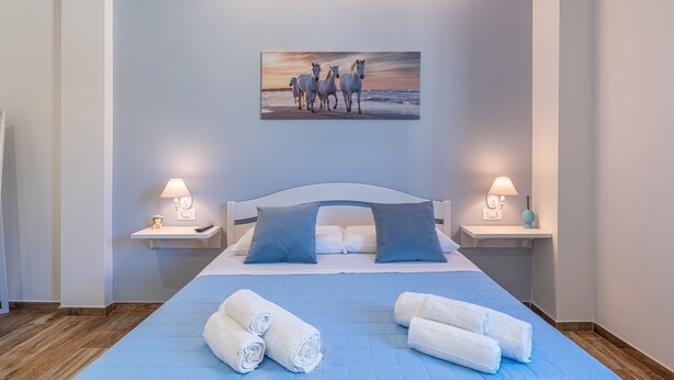 Quarto com cama, duas mesas de cabeceira, um quadro e toalhas dobradas.