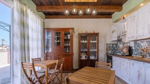 Ein Holzespeisesaal mit Stühlen, eine Küche mit weißen Schränken und ein großes Fenster mit Vorhängen.