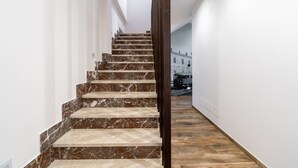 Eine Marmortreppe mit einem Holzgeländer führt zu einem Raum mit Holzboden und weißen Wänden.