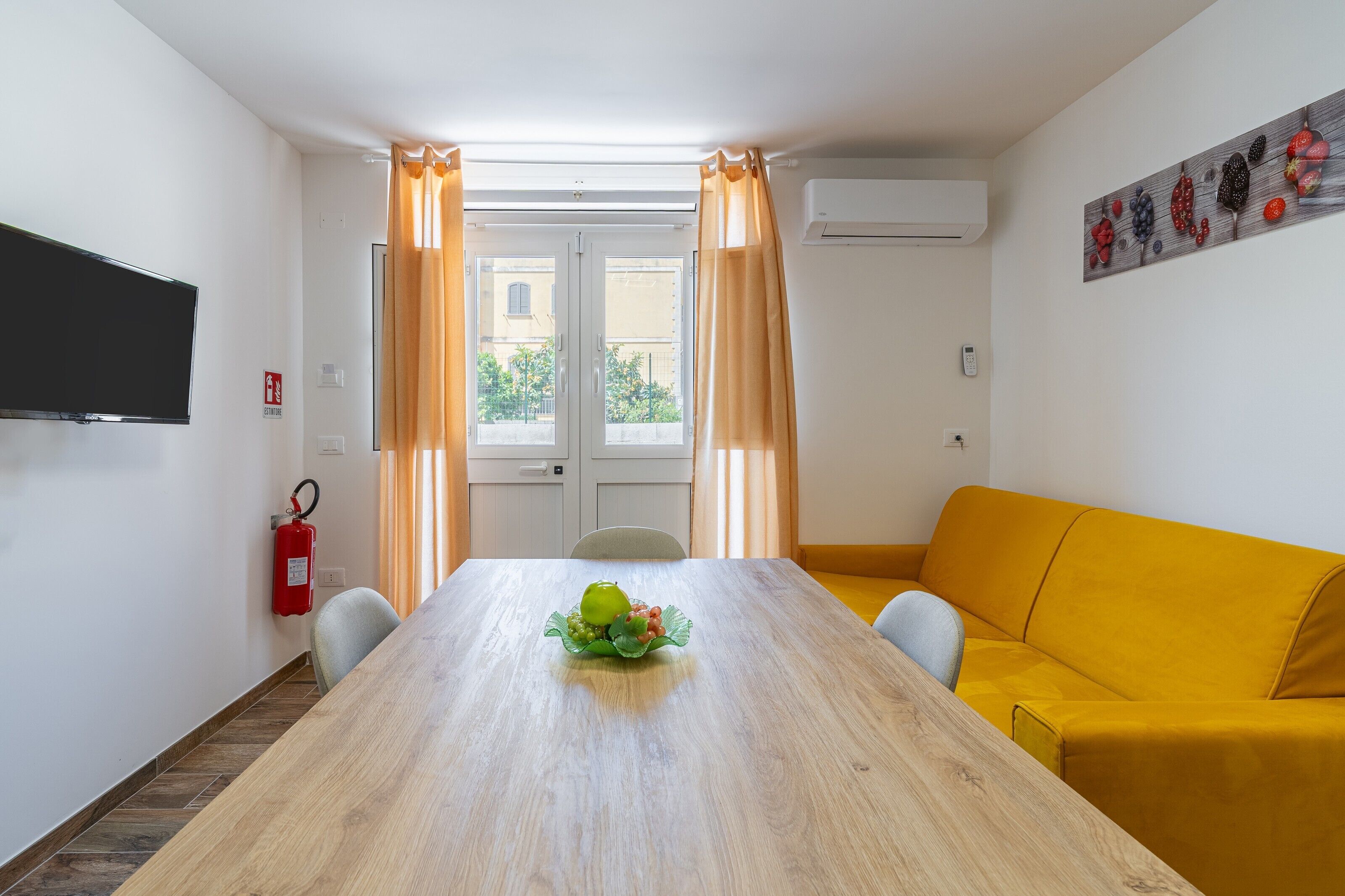 Una habitación con una mesa de madera, un sofá amarillo y un frutero.
