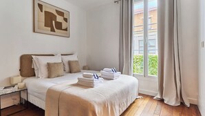 Ein ordentlich eingerichtetes Schlafzimmer mit Bett, Kissen, einem Nachttisch und einem Fenster mit Vorhängen.