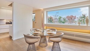 Ein moderner Essbereich mit einem Glastisch, Korbstühlen und Blick auf Bäume durch ein großes Fenster.
