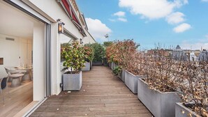 Eine Holzterrasse mit Blumentöpfen, ein Essbereich mit Stühlen und Tischen und ein Blick auf die Stadtlandschaft.