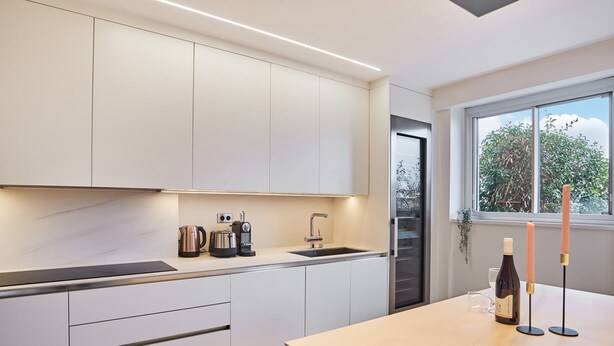 Eine moderne Küche mit weißen Schränken, einem eingebauten Backofen, einer Kaffeemaschine und einer Weinflasche auf der Arbeitsplatte.