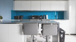 Una cucina moderna con mobili bianchi, una parete di fondo blu e un bancone con sgabelli.