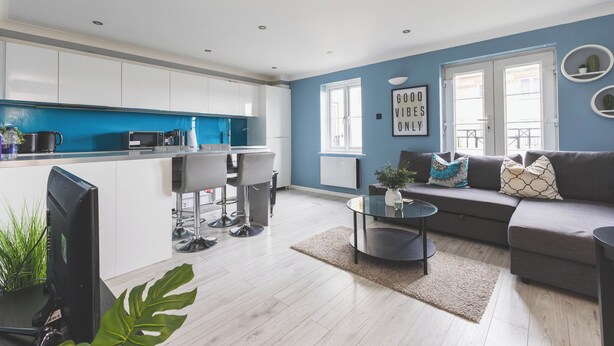 Un soggiorno moderno con un divano grigio, un tavolino da caffè e un angolo cottura con mobili bianchi e dettagli blu.