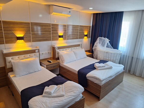 Habitación de hotel con dos camas, una cuna, aire acondicionado de pared y una ventana con cortinas.