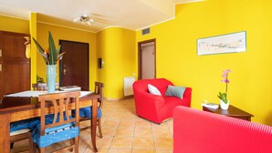 Un salon avec un canapé rouge, une table à manger avec des chaises, un vase rempli de fleurs et un tableau accroché au mur.