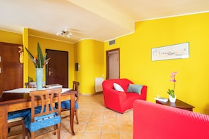 Ein Wohnzimmer mit rotem Sofa, einem Esstisch mit Stühlen, einer Blumenvase und einem Bild an der Wand.
