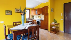Une cuisine avec des meubles de rangement en bois, une table à manger avec des chaises et une petite table d’appoint.