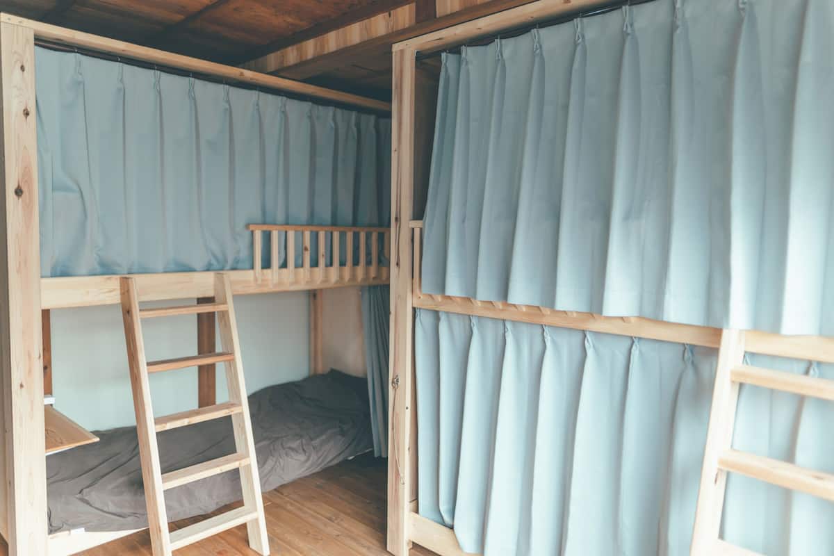A bunk bed room with a wooden ladder, a grey mattress, and light blue curtains.