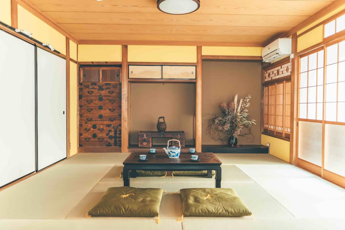 A traditional Japanese room with tatami flooring, a low table with a tea set, sliding doors, and a view through a shoji screen.