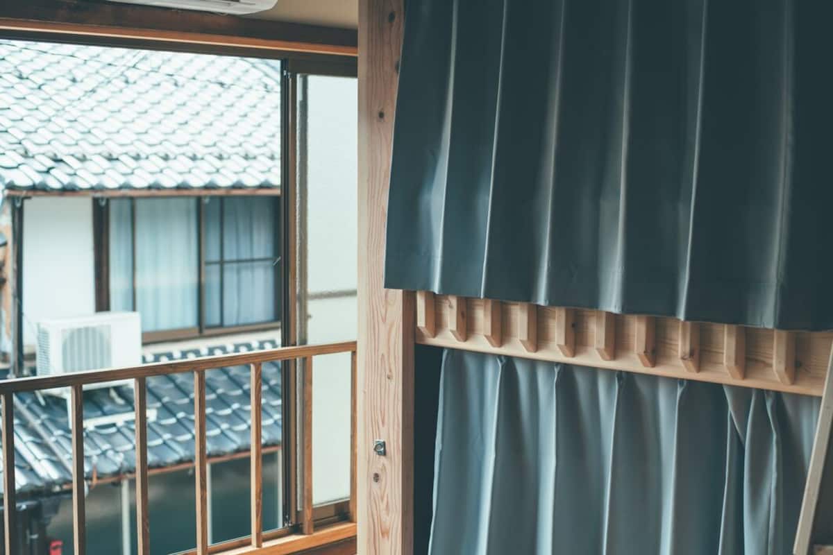 A room with a view of a traditional tiled roof outside, a wooden railing, and a curtain.
