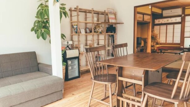 Un coin repas avec une table et des chaises en bois, un canapé gris et une bibliothèque contenant divers objets.