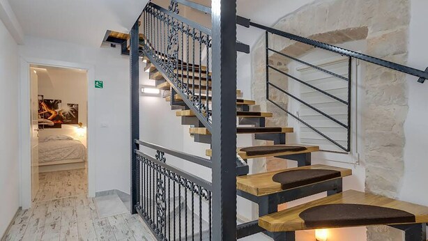 Una escalera con escalones de madera y barandillas de metal negro que conduce a un dormitorio con una cama y un cuadro en la pared.