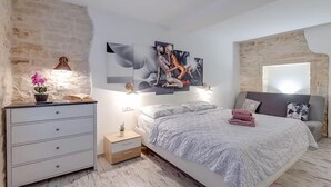 Un dormitorio con cama, mesitas de noche, lámpara, planta en maceta y obra de arte en la pared.